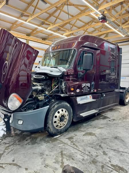 A burgundy semi truck with its hood up in a garage.