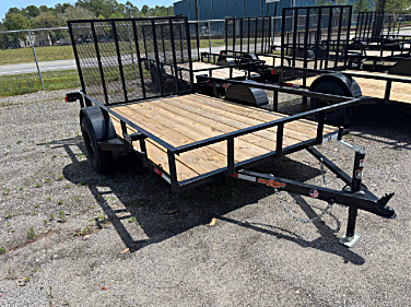 Black utility trailer with wooden deck and metal mesh sides, parked outside.