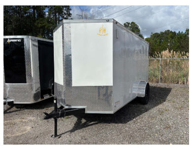 Enclosed silver cargo trailer with a blank white panel on its side. Outdoors on gravel.