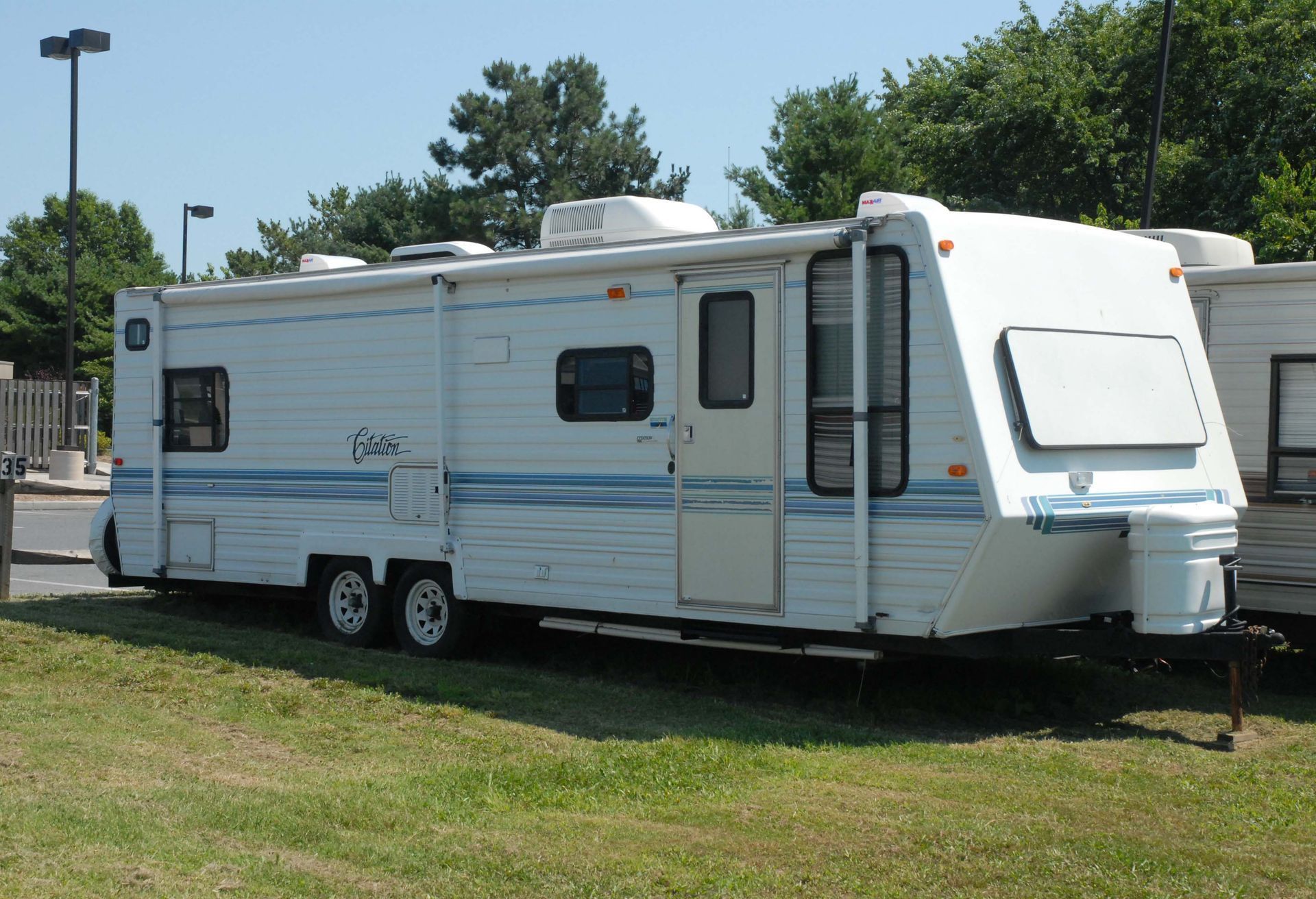 White travel trailer parked on grass, blue stripes, sunny day.