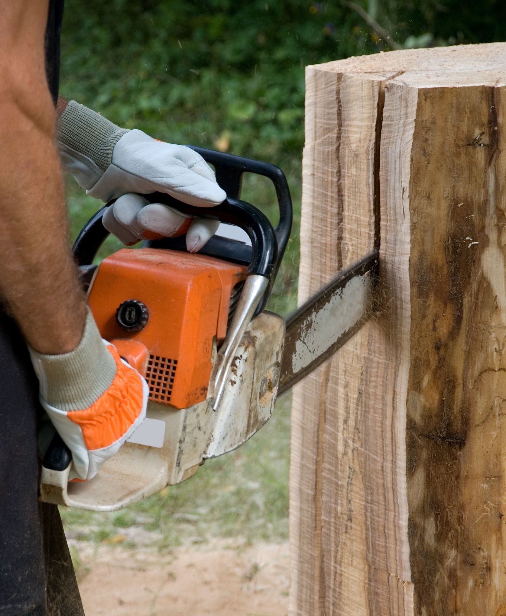 Person using an orange chainsaw to cut into a wooden log outdoors, wearing gloves.