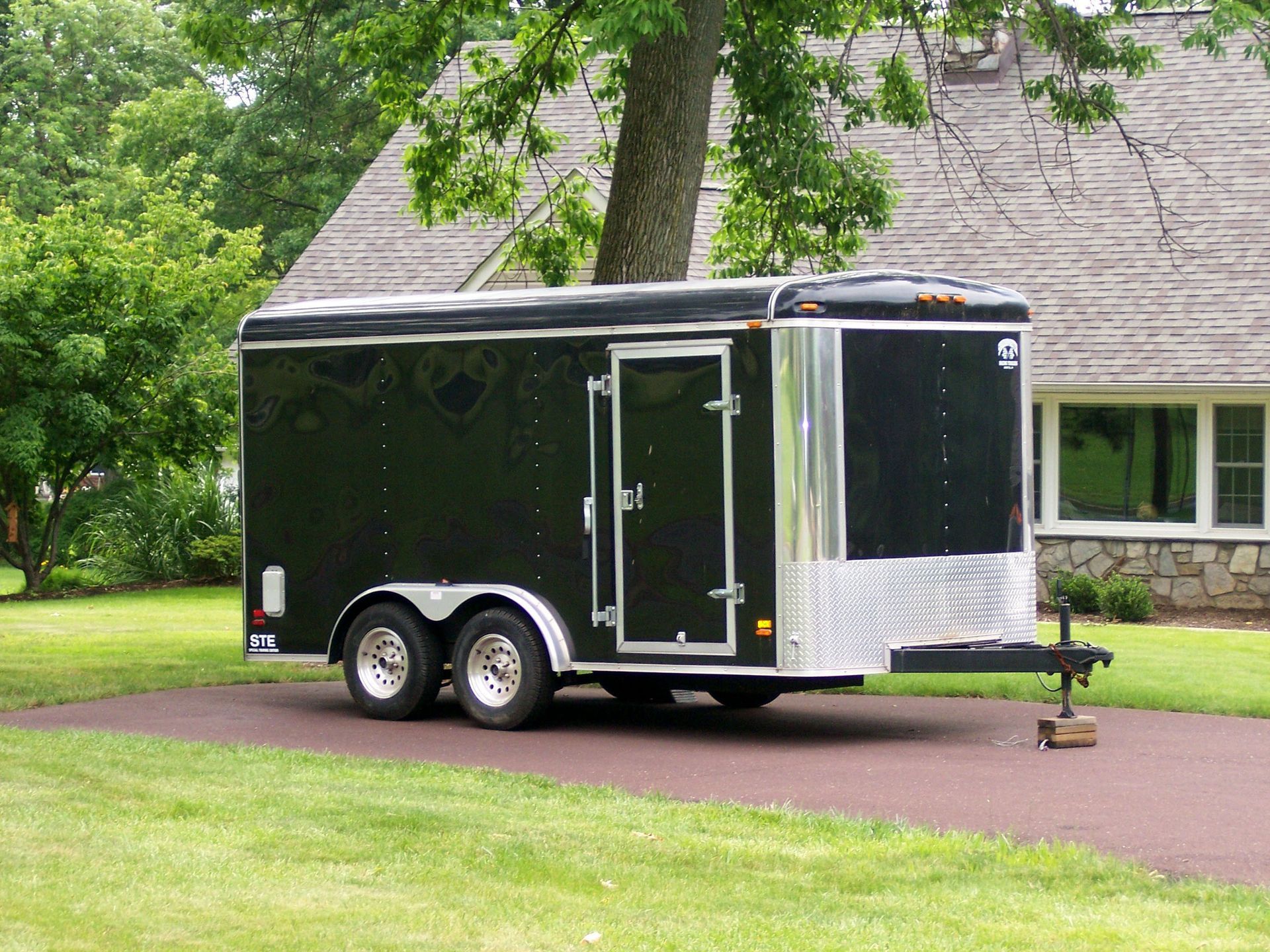 Black enclosed trailer parked on a driveway in front of a house.