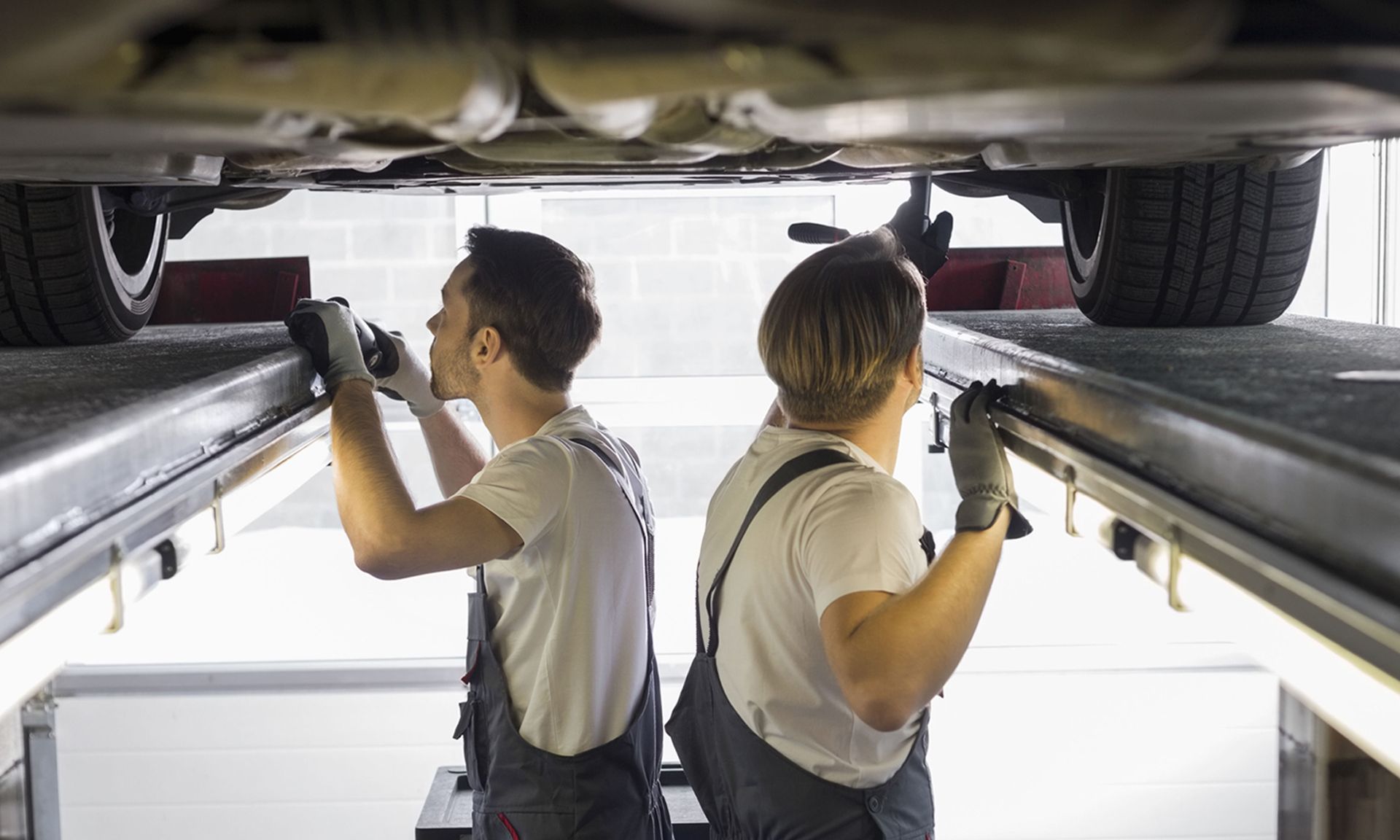 Two mechanics inspecting a car underside on a lift in a garage