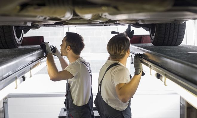 Two mechanics inspecting a vehicle’s undercarriage on a lift in an auto repair shop