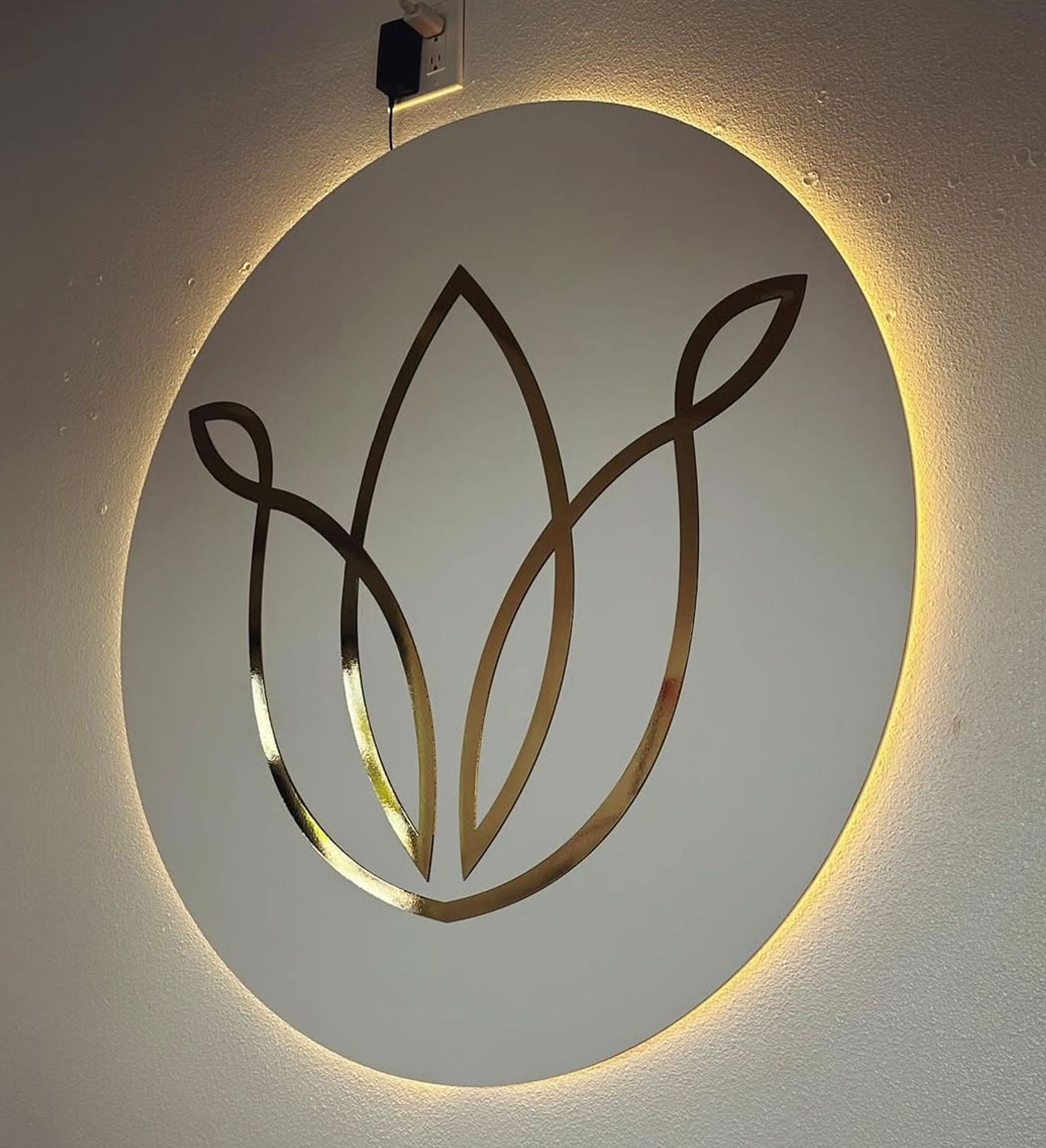 Gold floral logo on a white, backlit circular sign.