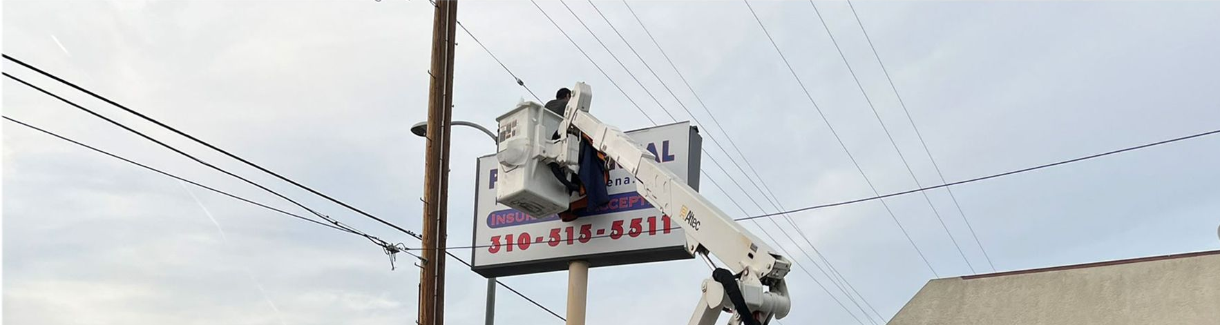 A utility truck lifts a worker to repair a sign on a pole under power lines.