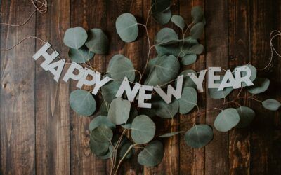 White “HAPPY NEW YEAR” letters on a wooden background with green eucalyptus leaves.