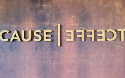 Mirror-reversed gold letters reading “CAUSE” on a textured purple wall