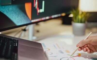 Hand drawing charts on paper beside a laptop and monitor in a workspace