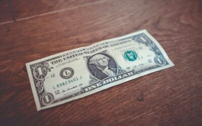 A one-dollar bill lying on a wooden table.