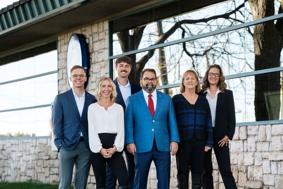Five people standing outside a building, dressed in business attire, posing for a group photo.