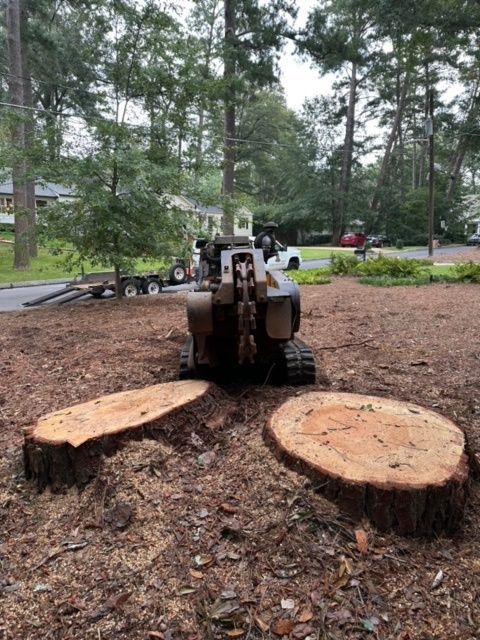 A tractor is cutting down a tree stump in a yard.