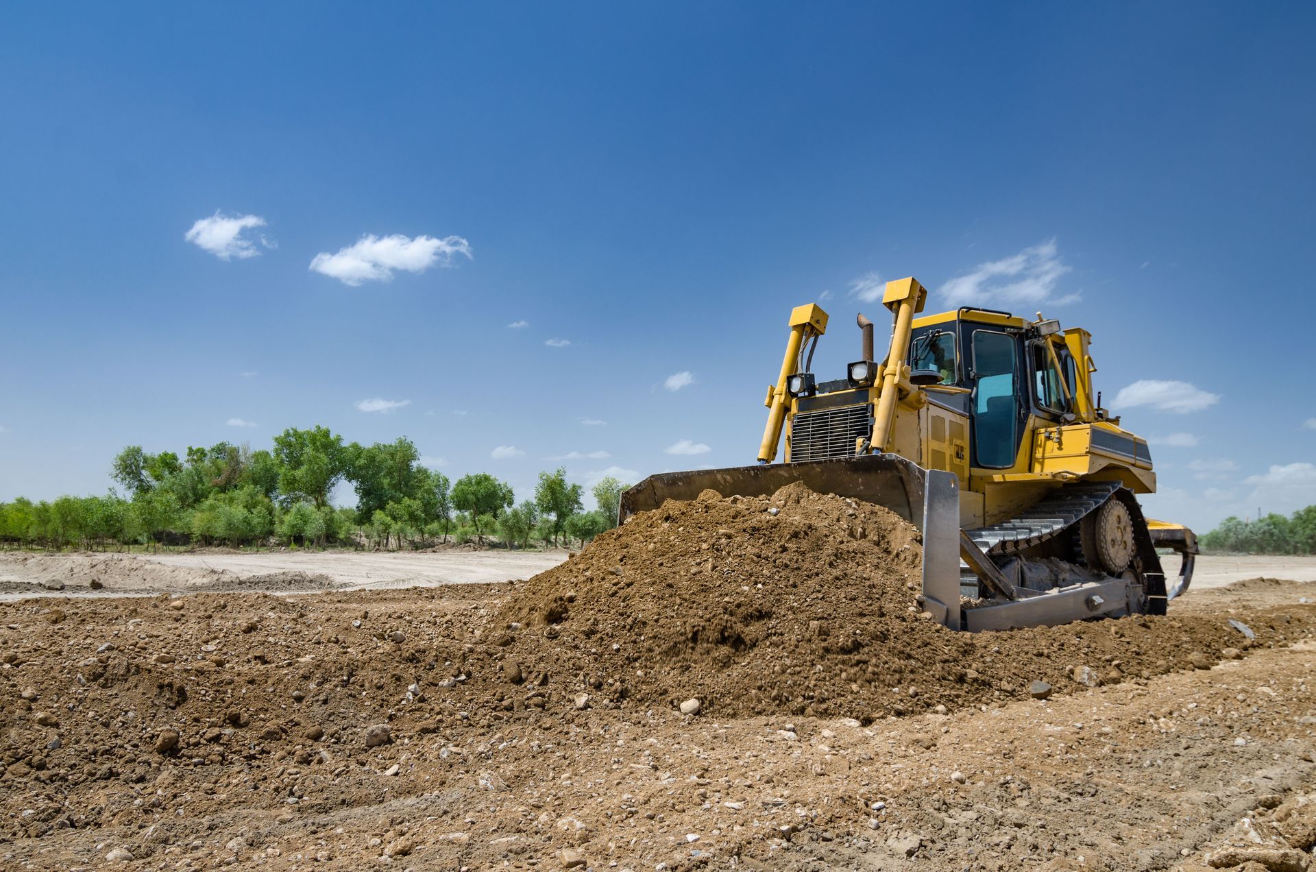 Yellow bulldozer pushing dirt on a construction site under a blue sky.