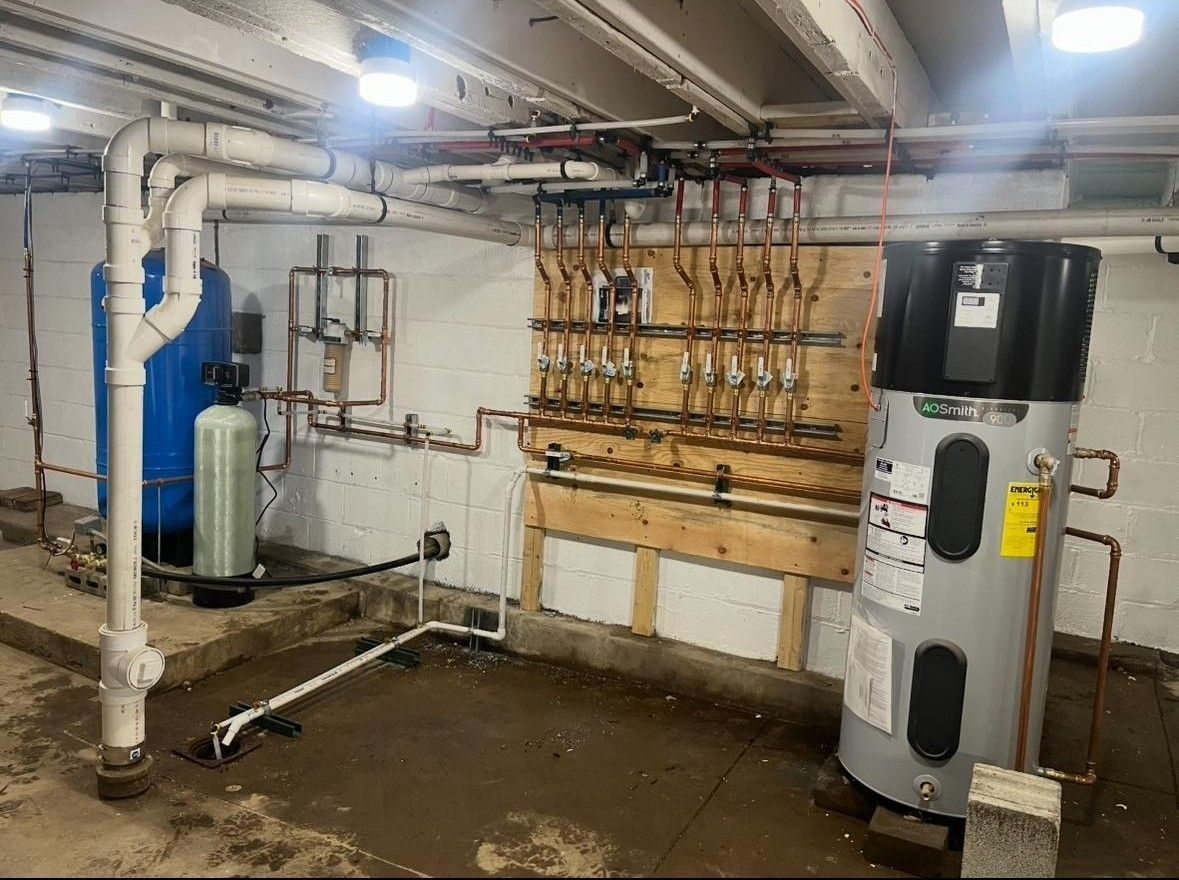 Basement utility room with pipes, valves, and water heaters against a concrete wall.