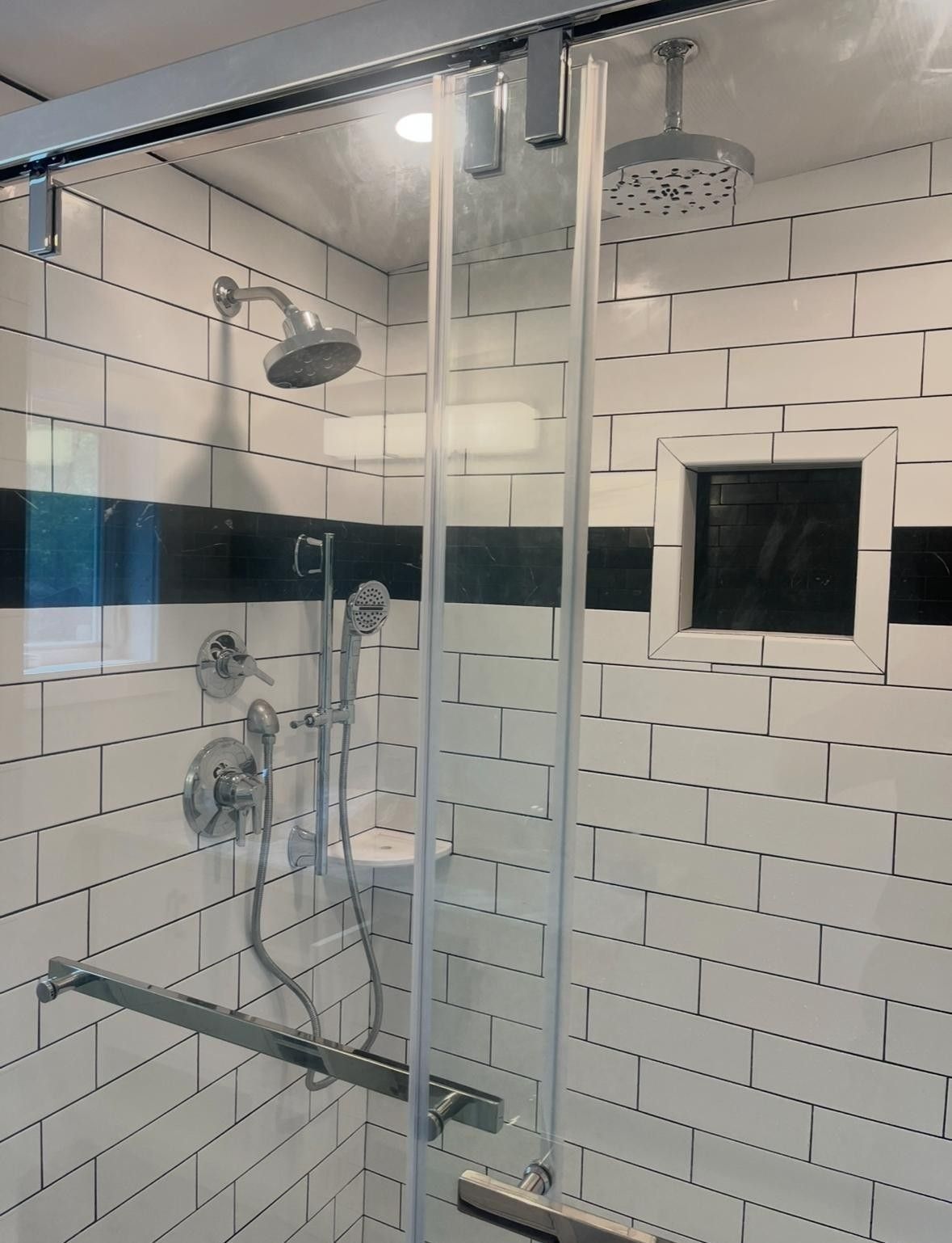 Glass shower stall with white subway tile walls, chrome fixtures, and a built-in bench.