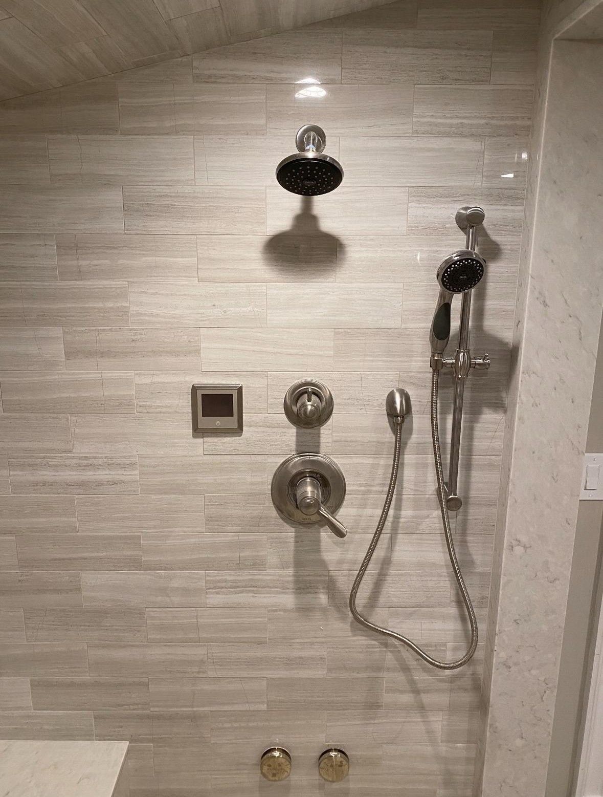 Tiled shower wall with chrome showerhead, handheld sprayer, and control valves
