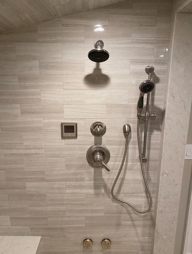 Tile shower with chrome fixtures, handheld sprayer, and overhead showerhead in a bathroom.