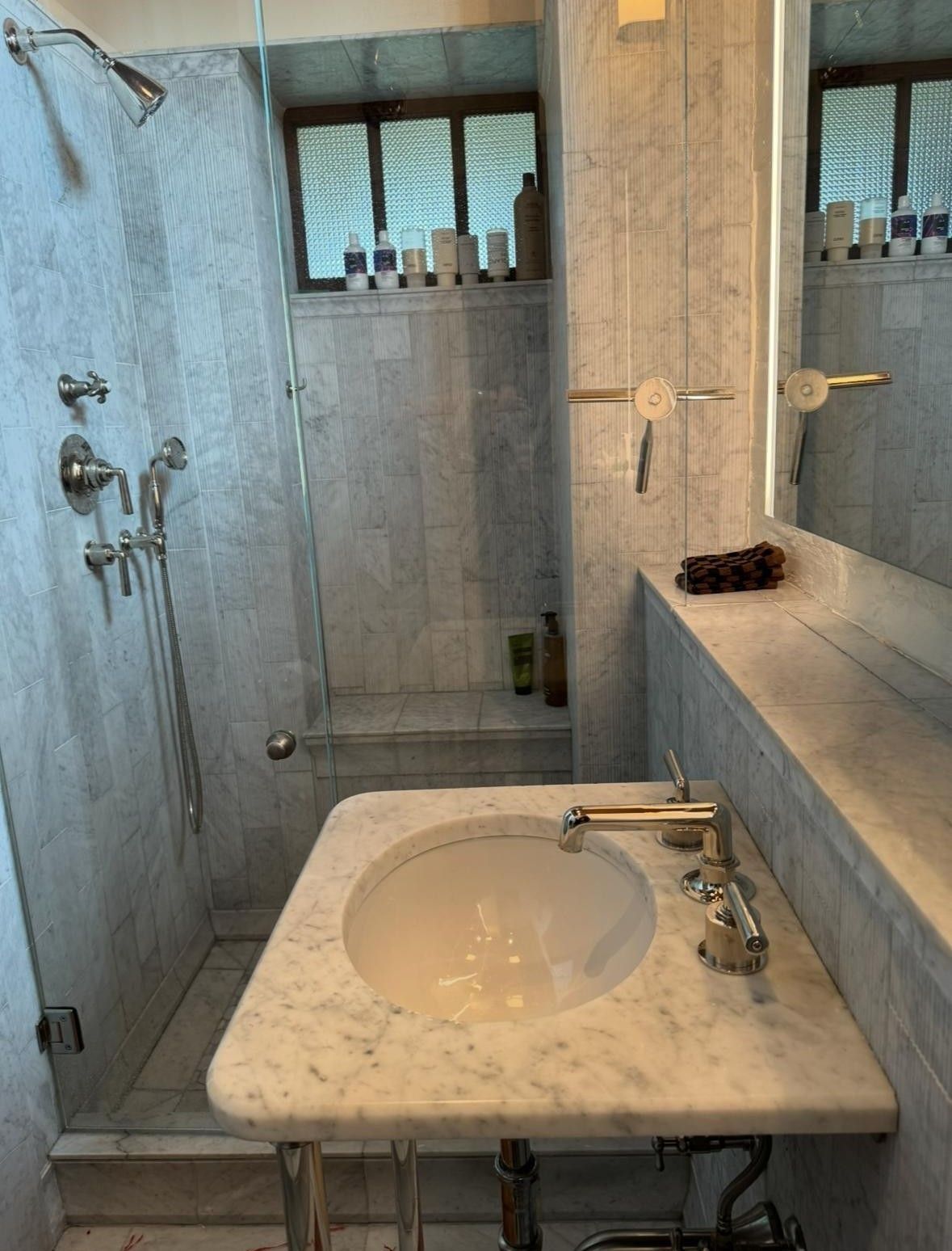 Small marble bathroom sink with mirror, gray tile walls, and shower visible in the background