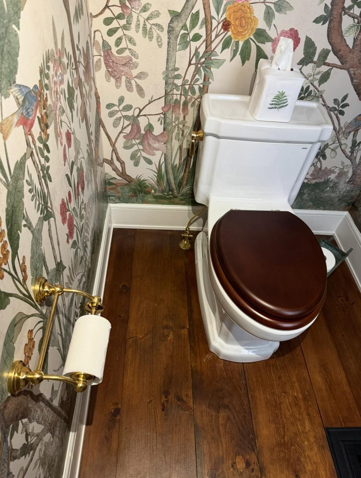 Small bathroom with a white toilet, dark wood floor, and floral wallpaper.