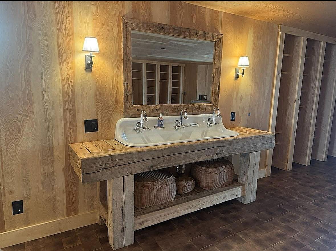 Rustic double-sink vanity with stone countertop, mirror, wall sconces, and baskets underneath in a tiled room