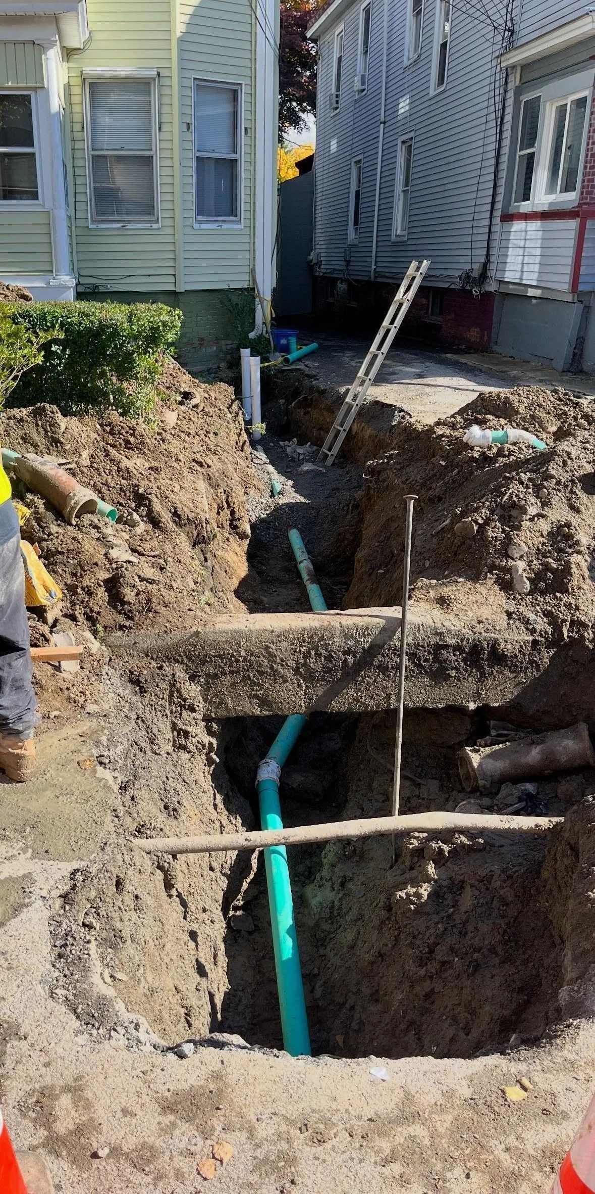 Open trench between houses with a green pipe and wooden supports at a construction site