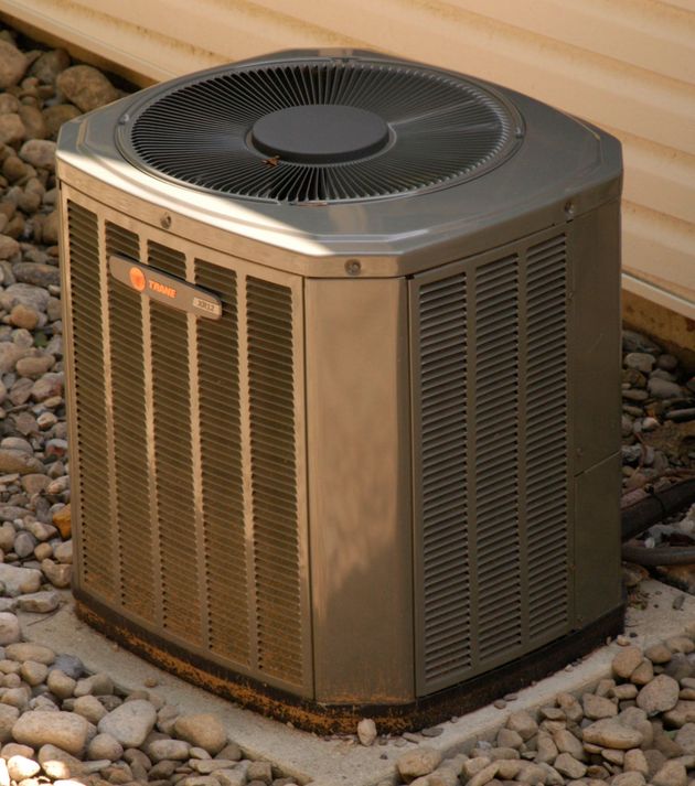 Outdoor central air conditioning unit on a gravel bed beside a house.