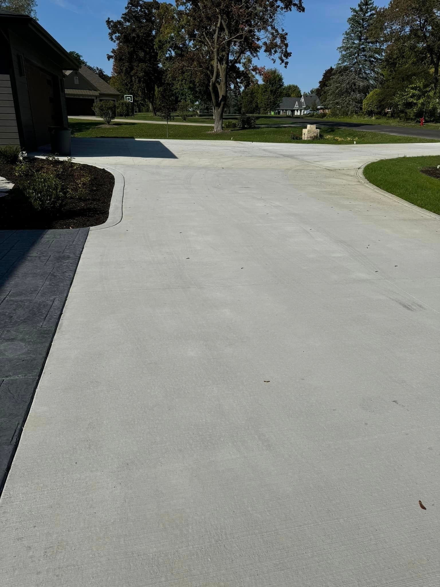 A paved driveway stretches from the foreground toward a garage and grassy yard under a bright, clear blue sky.