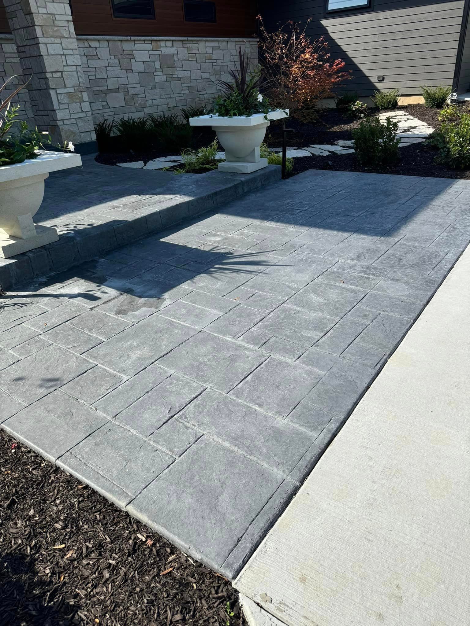 A grey, rectangular paver walkway leads to a raised stone-walled landing with large white planters.