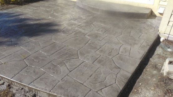 A gray concrete patio with an irregular, stamped stone pattern leading up to a curved entrance step.