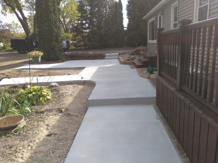 Concrete walkway beside a house with raised edging and a brown fence, leading through a landscaped yard