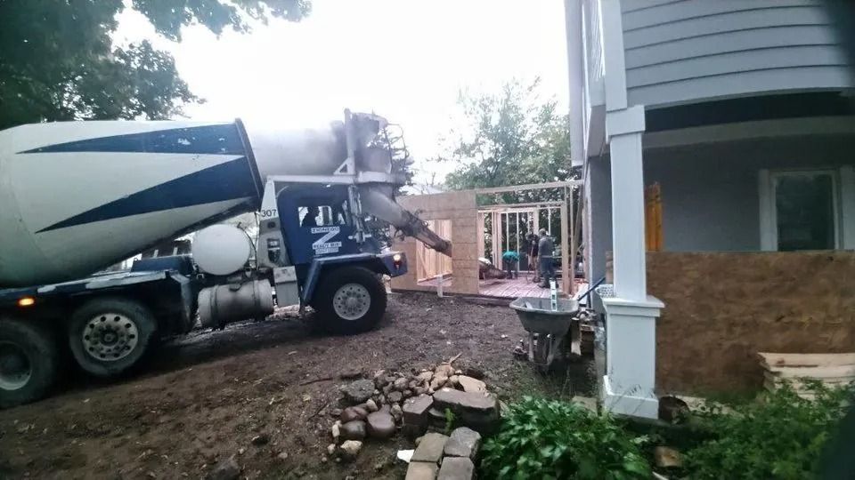 Cement mixer truck pouring concrete beside a house under construction in a muddy yard