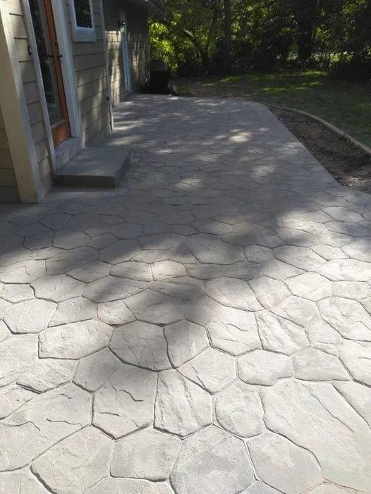 Stone-patterned walkway beside a building, leading into a shaded yard with trees.