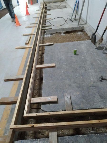 Wooden concrete formwork installed on a construction site floor near a trench and scattered tools.