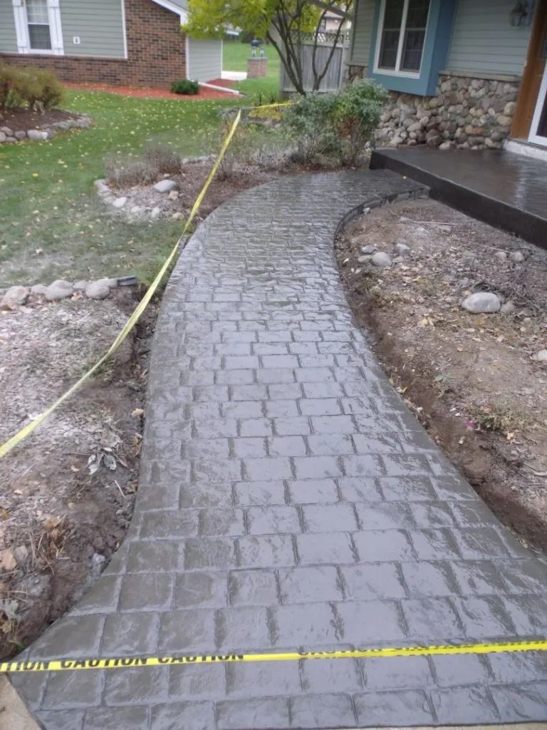 Curved brick walkway under construction beside a house, lined with yellow caution tape.
