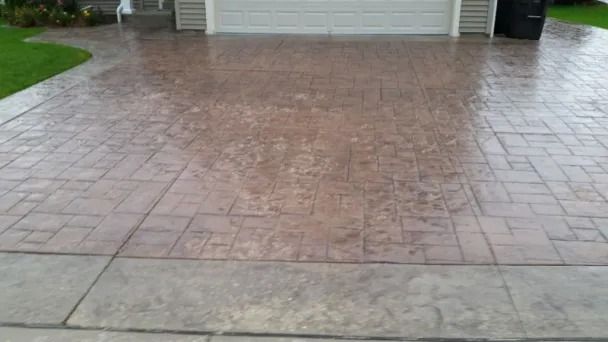 Rain-soaked stamped concrete driveway in front of a garage, with wet sidewalk in the foreground