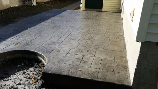 Stamped concrete patio beside a house, with a circular fire pit in the foreground.