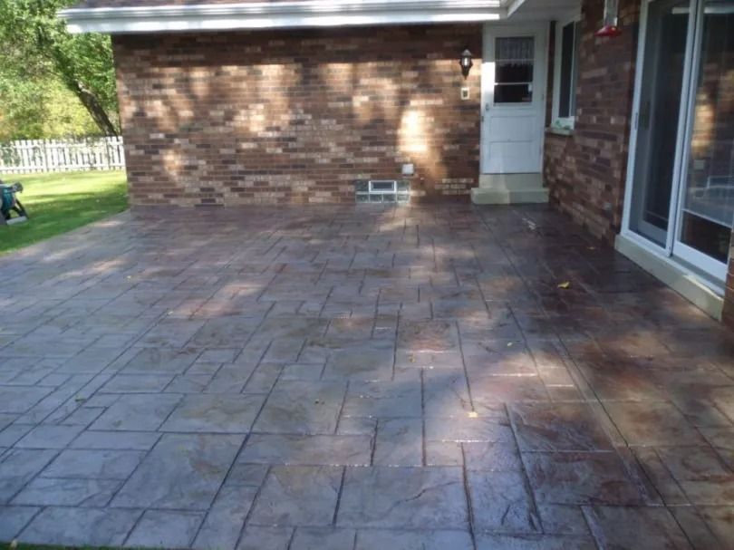 Stamped concrete patio beside a brick house with sliding glass doors and a white side door.
