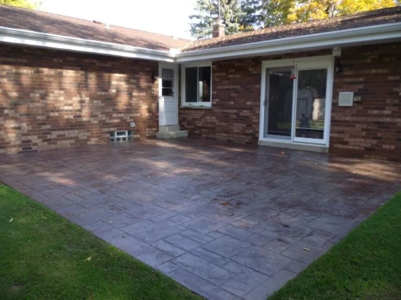 Brick patio beside a house with sliding glass doors and a small grass lawn.
