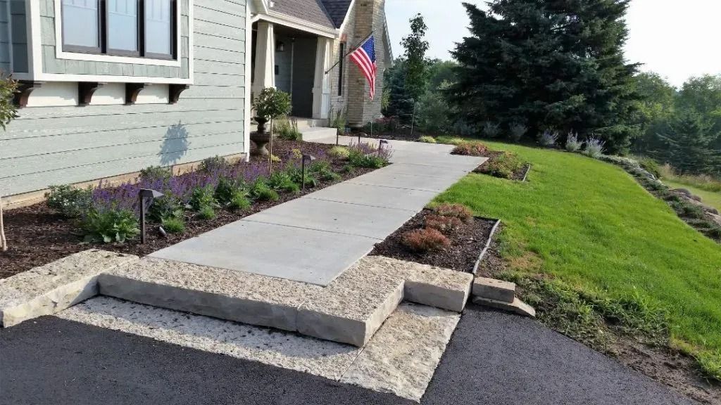 Concrete accessibility ramp leading to a house entrance, with landscaping and an American flag nearby