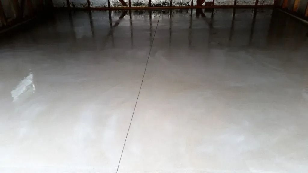 A freshly poured, smooth grey concrete floor in an unfinished room with wooden wall framing in the background.