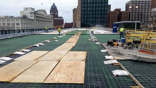 Construction workers on a city rooftop installing a green roofing system with wooden walkways and materials.