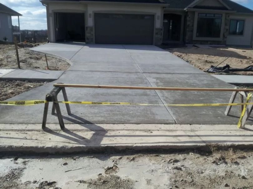 New concrete driveway under construction with caution tape and metal barricades in front of a house
