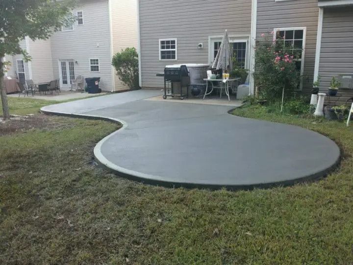 Curved concrete patio in a backyard beside a house, with outdoor furniture and a small garden bed.