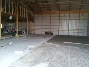 Interior view of a large unfinished building with concrete floors, wooden wall framing, and metal siding panels.