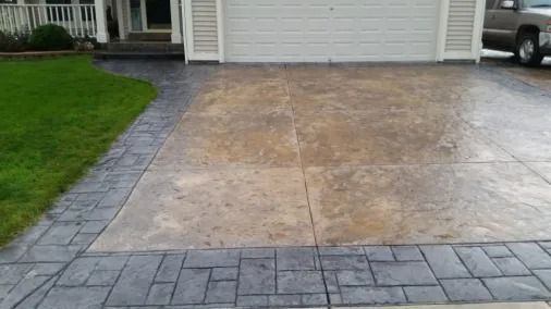 Concrete driveway with a brick border leading to a white garage, beside a green lawn.