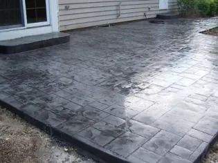 Stamped concrete patio beside a house, wet and glossy after rain.