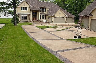 Suburban house with a long concrete driveway, green lawn, and a detached garage.