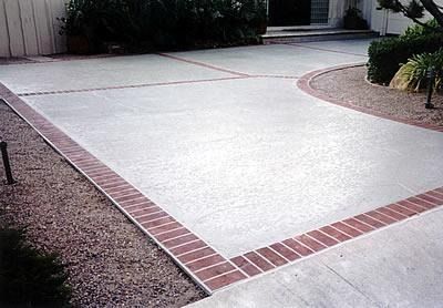 Curved concrete driveway bordered by red brick edging beside a landscaped yard and house entrance