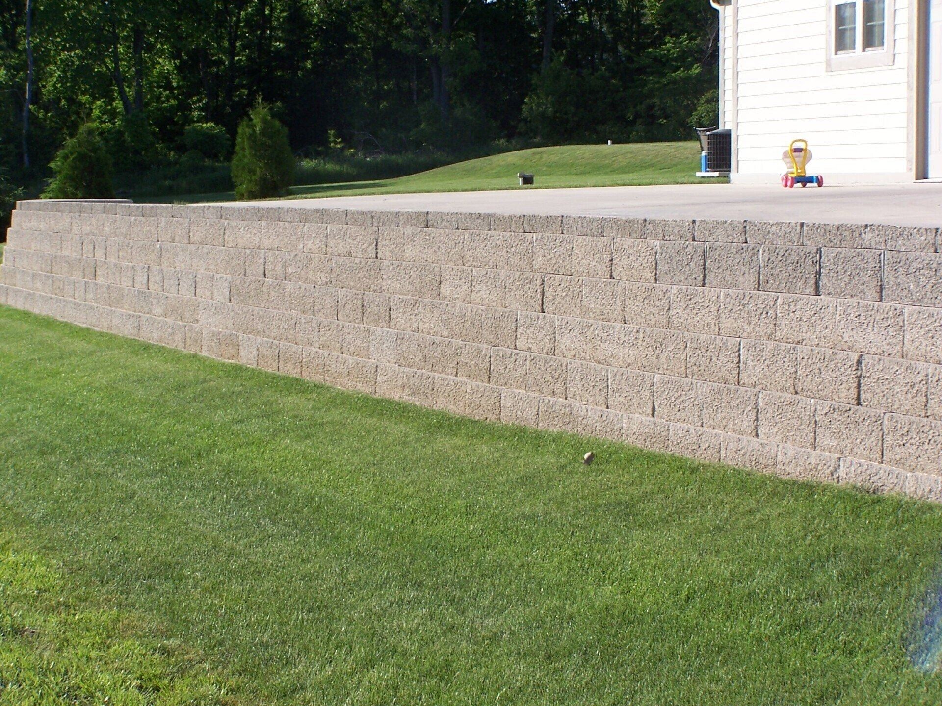 Long stone retaining wall beside a grassy lawn near a white house.