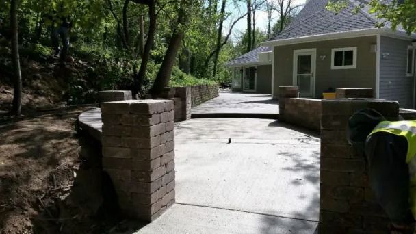 A concrete patio under construction with brick pillars and a retaining wall, leading toward a house exterior.